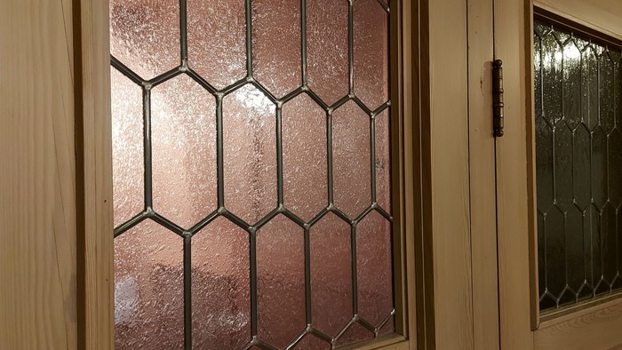 Dekorative Tür aus wabenförmigem Buntglas mit Holzrahmen und angrenzender Metalltür.