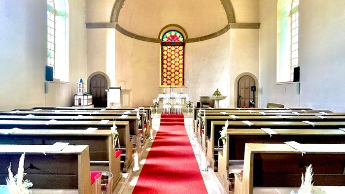 Kircheneingang mit roter Teppichbahn und Holzbänken