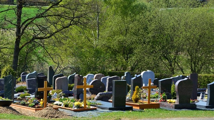 Ein friedlicher Friedhof mit zahlreichen Grabsteinen und Blumen, umgeben von üppigem Grün.
