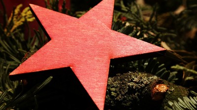 En stor rød stjerne på en mørk underlag med smykker og grønne planter.