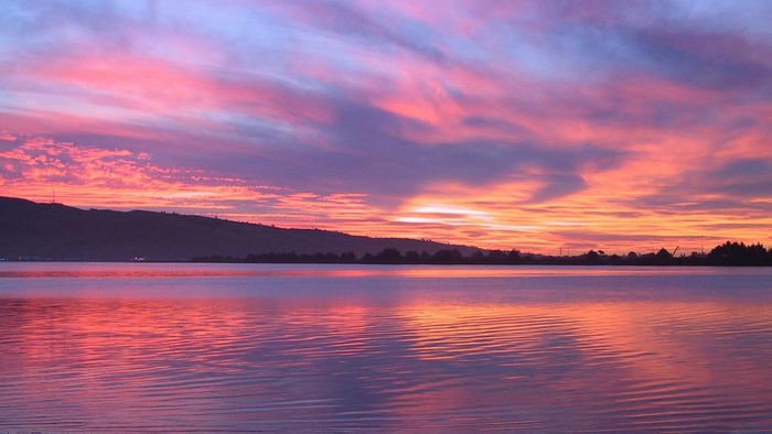 Solnedgang over rolig sø med spejling