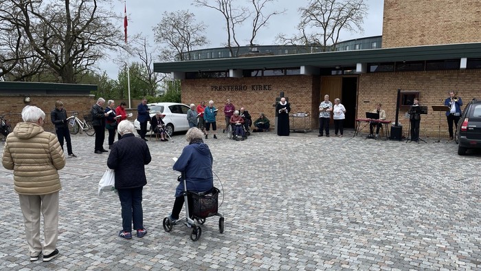 En gruppe mennesker står udenfor et murstensbygning, nogle med rullestoler og køler.