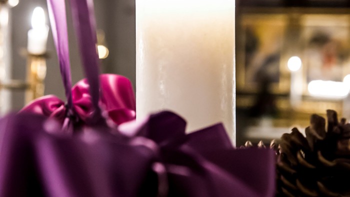 En lysende hvid lysestage med mørkeviolett bånd og nødder i forgrunden