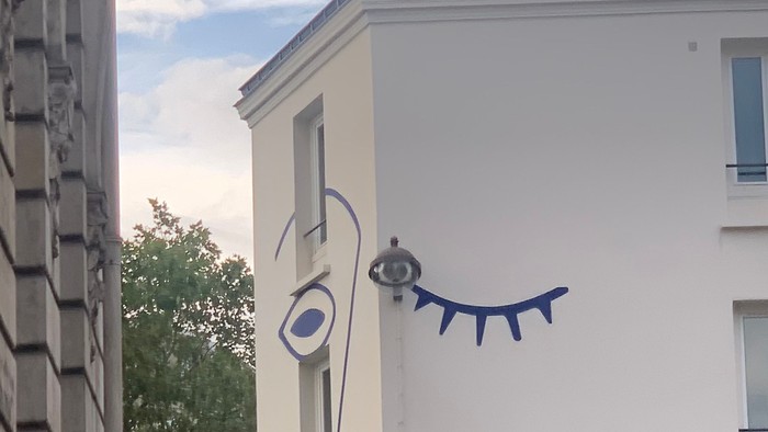 En blå og hvid tegnelse af et øje og en snak på siden af et hvidt bygning.