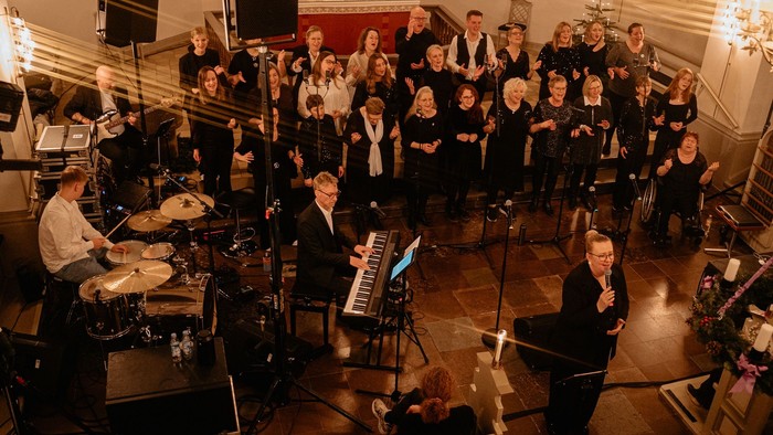 En stor gruppe af musikere og sanger på scenen med instrumenter og noter