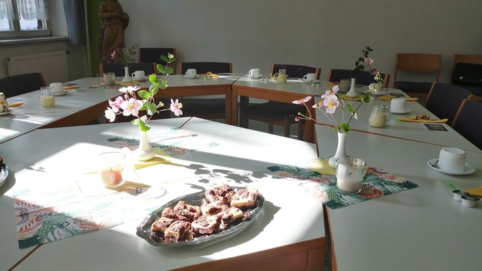 Ein helles Zimmer mit mehreren Tischen, die mit Blumen, Geschirr und Gebäck gedeckt sind