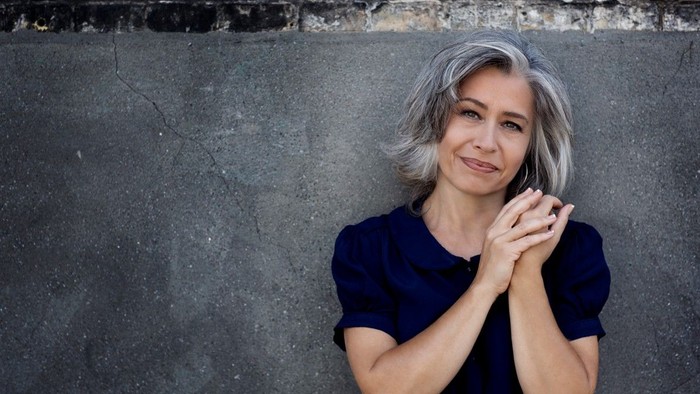 En kvinde med kort, grå hår sidder med hænderne samlet foran ansigtet.