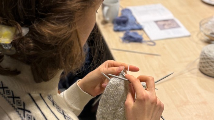 En person, der omhyggeligt broderer eller syr i hånden på et strikket stof ved et håndarbejdsbord.