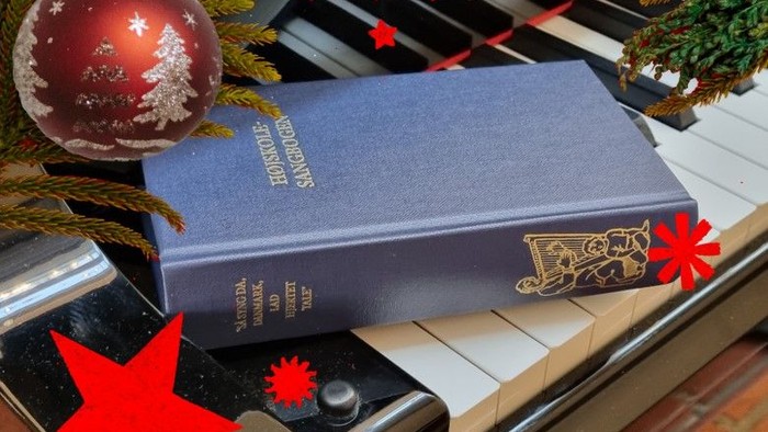 Blå bog med guldindskrift på piano med juldekorationer