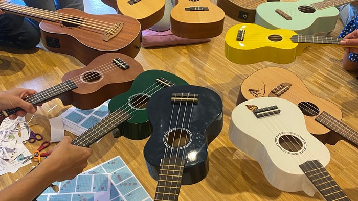 Eine Gruppe von Menschen spielt verschiedene Ukulelen auf einem Holzboden