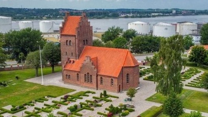 En rød murstenskirke med høje tårne og en velholdt have med buske og træer.