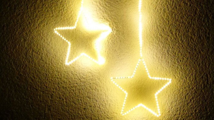 Zwei leuchtende Sterne hängen vor einem Fenster mit Weihnachtsbeleuchtung, Fenster-Adventskalender Weckartshain