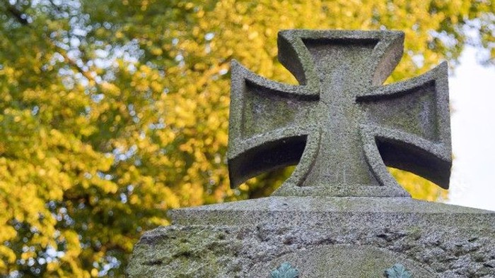 Ein steinernes Kreuz mit Verzierungen auf einem Grabmal.