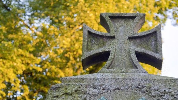 Ein steinernes Kreuz mit Verzierungen auf einem Grabmal.