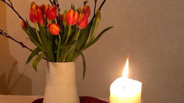 Eine Vase mit Tulpen und brennenden Kerzen auf einer gemütlichen roten Unterlage, akzentuiert durch Grünpflanzen.