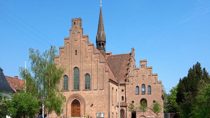 En stor, gotisk kirke med to tårne og spiret, bygget af røde mursten.