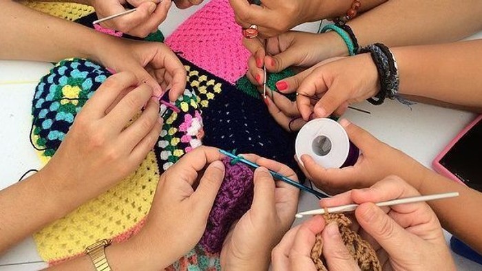 En gruppe af hände arbejder med strå og knipling på et bord.