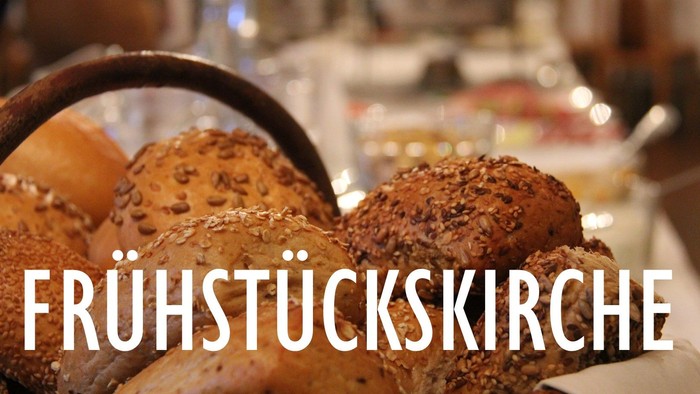 Ein Korb mit verschiedenen Broten und Brötchen, im Hintergrund ein Buffet mit Gläsern und Flaschen.