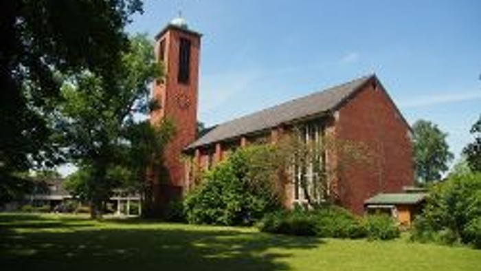Ein rotes Backsteingebäude mit zwei Türmen steht auf einem grünen Rasen unter einem klaren blauen Himmel.