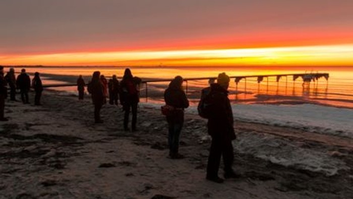 En gruppe mennesker går på stranden ved solopgang