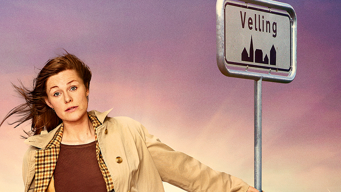 En kvinde i frakke står nær et gadeskilt med teksten 