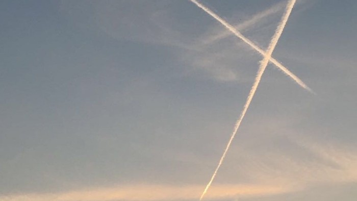 Ein Kirchturm vor einem Himmel mit Sonnenuntergang und Kondensstreifen
