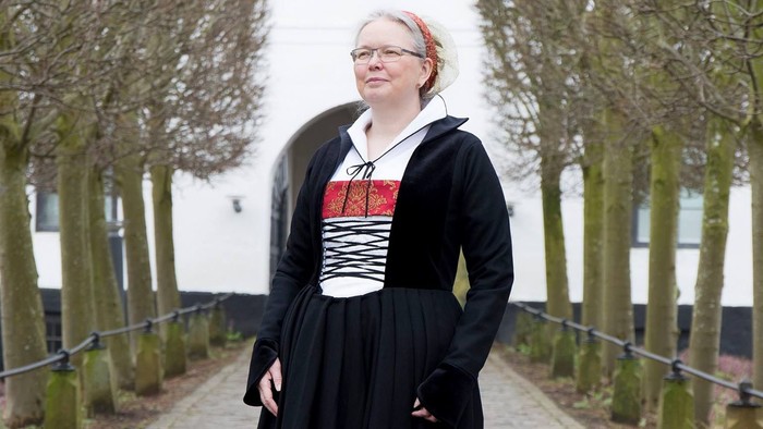 Kvinde i sort kjole med rød og hvid top, der står på en brostensbelagt sti.