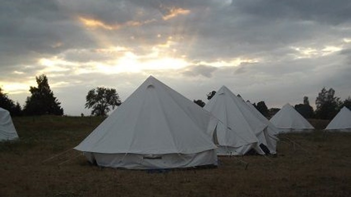 Mehrere weiße Zelte auf einem Feld bei Sonnenuntergang
