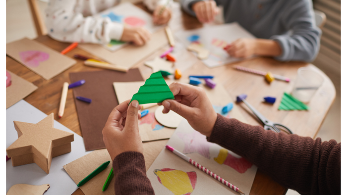 Kinder basteln mit buntem Papier und Kleber an einem Tisch.