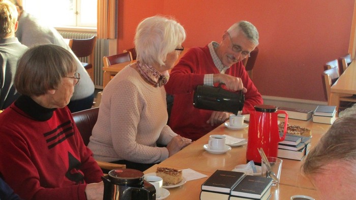 En gruppe ældre mennesker, der sidder rundt om et bord med kaffe og bøger.