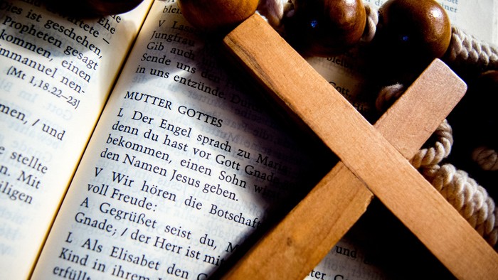 Holzkreuz auf aufgeschlagenem Buch mit Text in deutscher Sprache