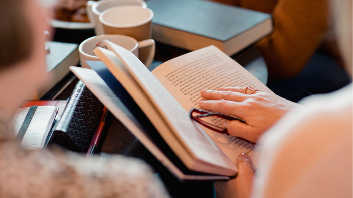 En person læser en åben bog, mens de holder en kop kaffe ved et hyggeligt bord.