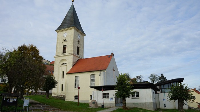 Kirchturm mit spitzem Dach und Uhr an einem weißen Kirchengebäude mit rotem Ziegeldach