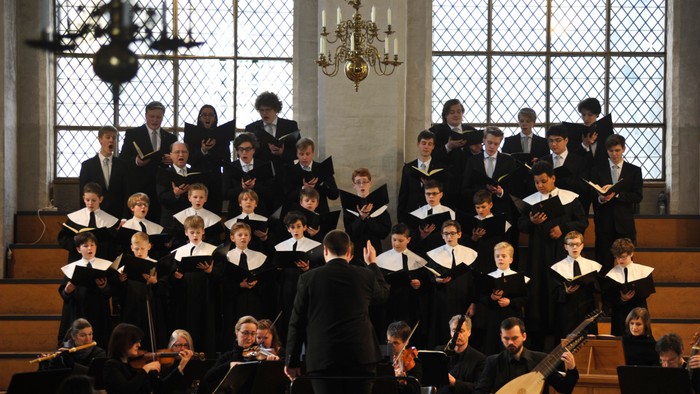 Ein großer Chor und ein Orchester treten gemeinsam in einer prächtigen, historischen Kirche auf.