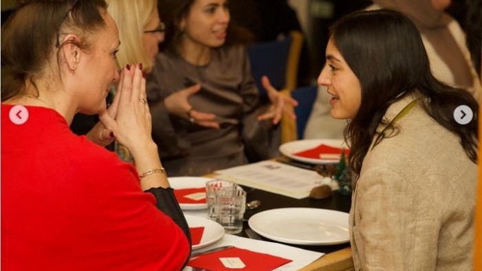 To kvinder i samtale ved en restaurantbord med andre i baggrunden.