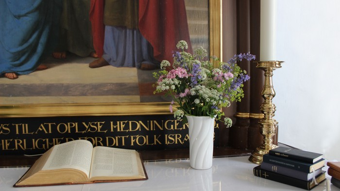 En hvid vase med blomster står på en hvid bord med en åben bog og en stabel bøger ved siden af