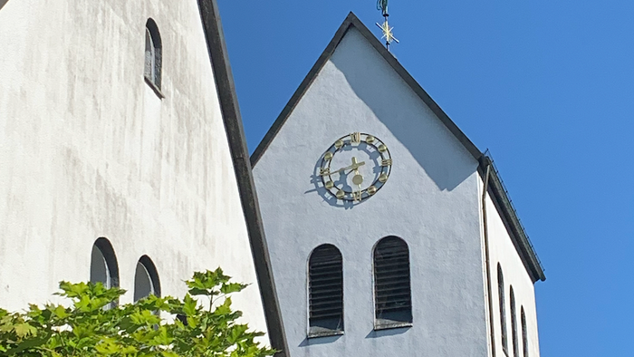 Weiße Kirche mit Uhr und Kreuz unter blauem Himmel