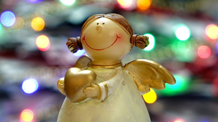 En lille engel-figur med guldvinger og et guld hjerte foran en lyssjæld.