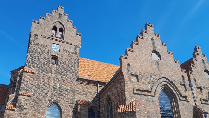 Gamle teglsteinskirke med spisse tårn og buevinduer under klar blå himmel