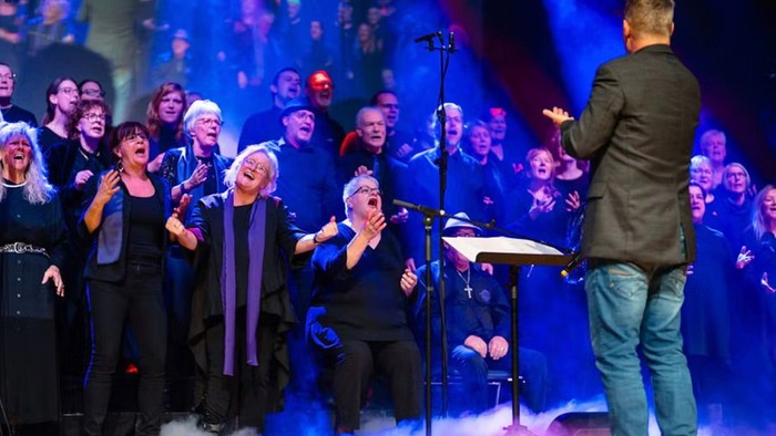 Et kor optræder på scenen med en dirigent, der leder dem.