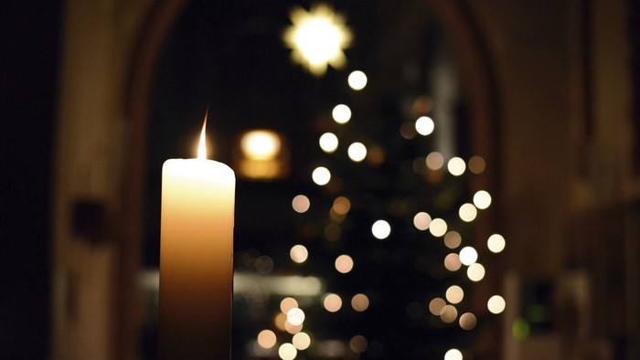 Eine brennende Kerze vor einem beleuchteten Weihnachtsbaum in einer Kirche.