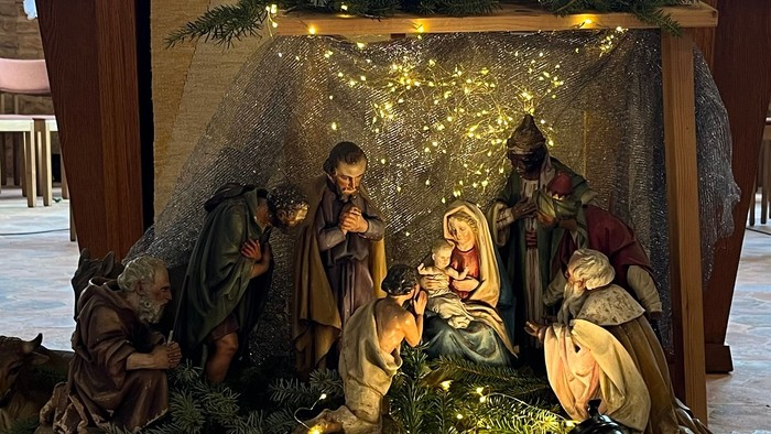 Eine Krippe mit Figuren, beleuchtet mit Lichtern und Tannenzweigen.
