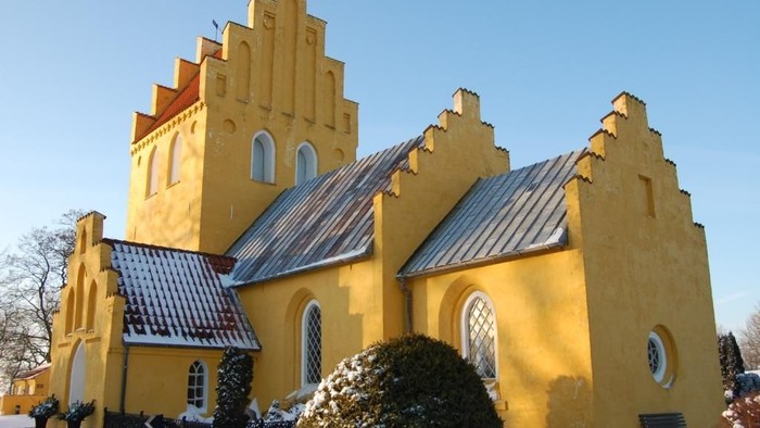 Gul kirke med spisse tårne og blå tag i sne.