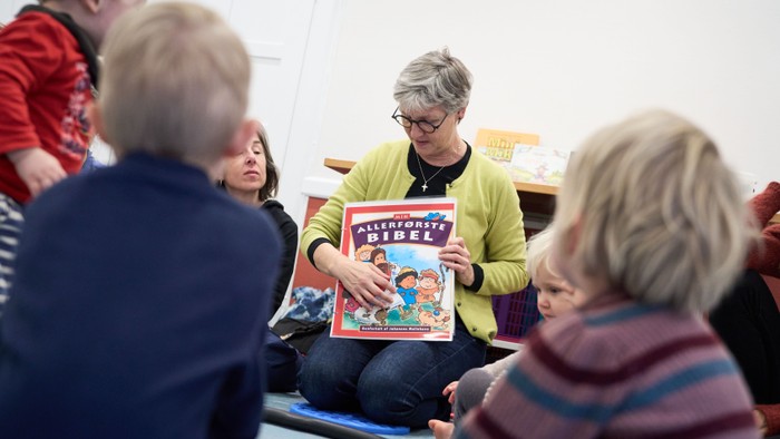 En kvinde læser et børnebog til en gruppe børn.