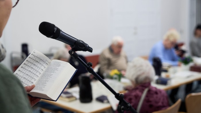En person læser ud af en bog ved et mikrofon, mens andre sidder og lytter.