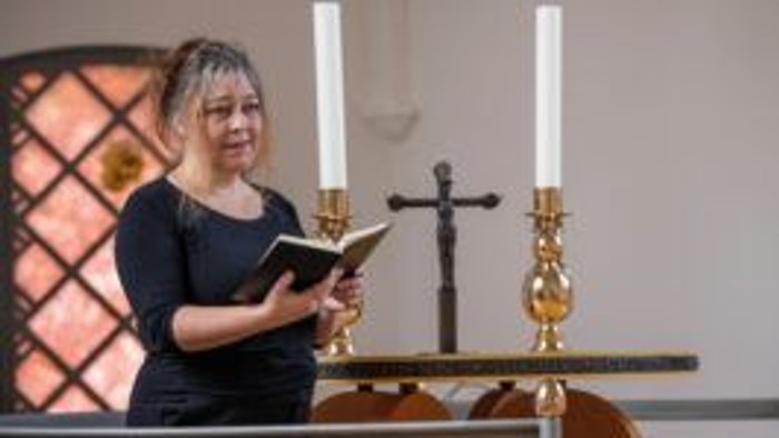 En kvinde læser fra en bog foran et kors og lys.