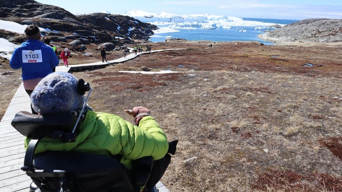 Person i kørestol betragter bjerglandskab med hav.