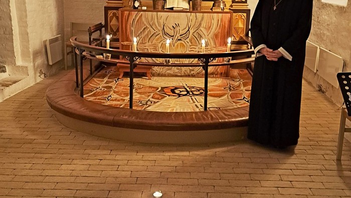 Nonne, der står foran et religiøst alter med et kors på gulvet.