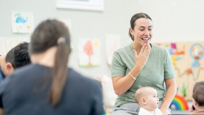 Eine Gruppe von Erwachsenen und Babys sitzt im Kreis auf dem Boden und beschäftigt sich mit einer spielerischen Aktivität.