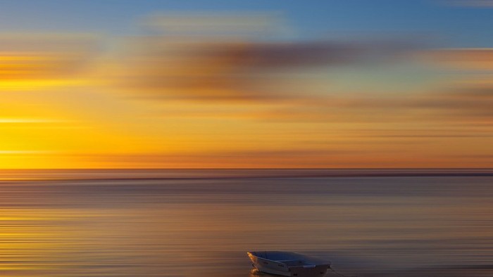 En blå båd på stranden ved en solopgang